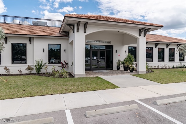 property entrance featuring french doors, a lawn, a tiled roof, and stucco siding