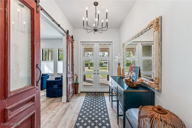 doorway to outside with light wood-style floors, a barn door, a chandelier, and french doors