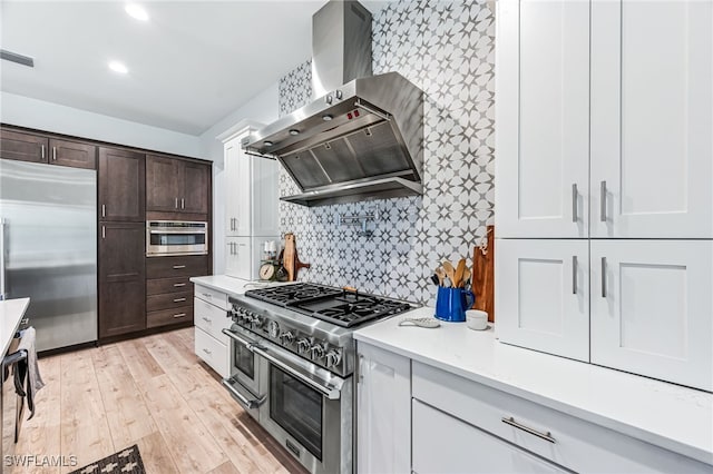 kitchen featuring high end appliances, visible vents, dark brown cabinetry, light wood-type flooring, and wall chimney exhaust hood