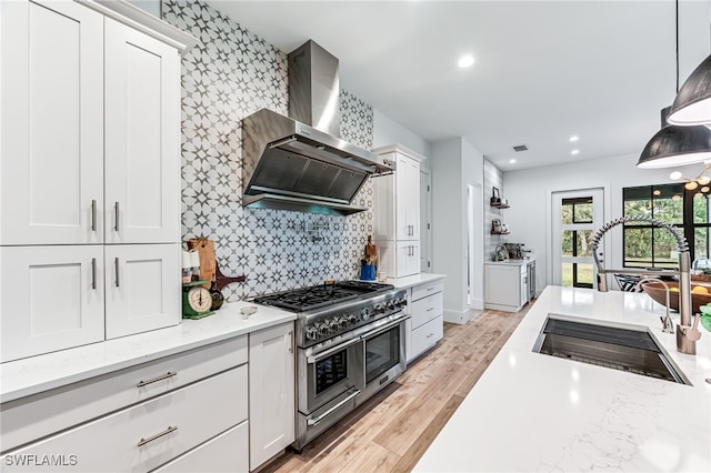 kitchen featuring range with two ovens, a sink, white cabinetry, wall chimney exhaust hood, and light wood finished floors