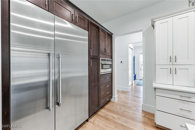 kitchen with dark brown cabinetry, baseboards, light countertops, appliances with stainless steel finishes, and light wood-type flooring