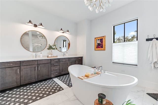 full bath featuring marble finish floor, double vanity, a chandelier, a freestanding tub, and baseboards