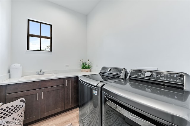 laundry area with light wood-type flooring, washing machine and dryer, cabinet space, and a sink