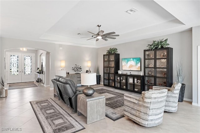 living area featuring arched walkways, light tile patterned floors, visible vents, french doors, and a tray ceiling