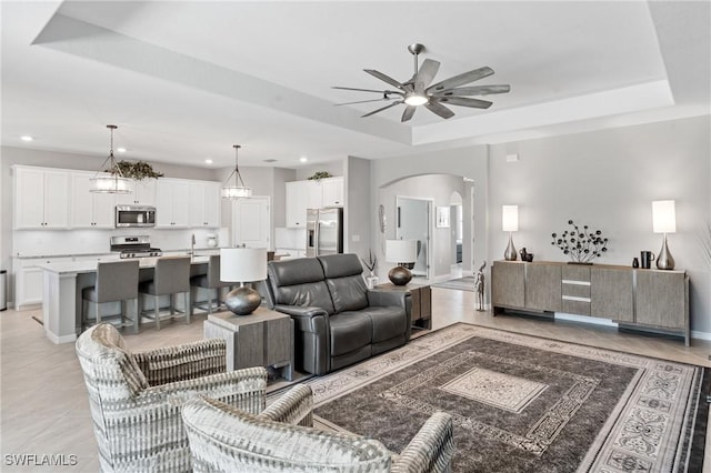 living area with baseboards, arched walkways, a ceiling fan, a tray ceiling, and recessed lighting