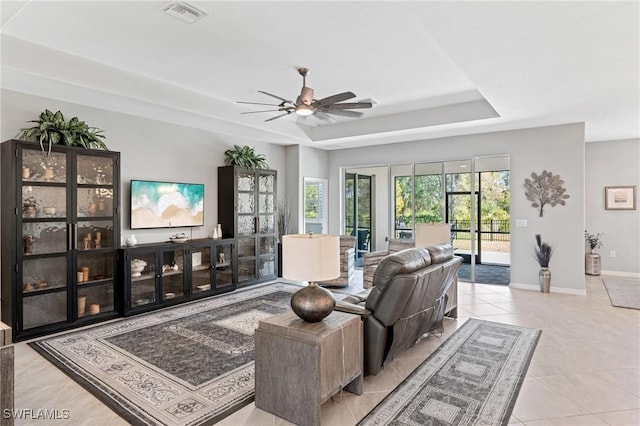 living room featuring tile patterned flooring, a ceiling fan, visible vents, baseboards, and a tray ceiling