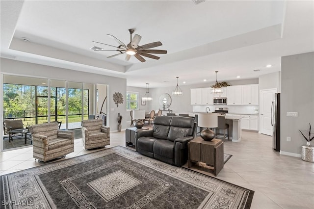 living room with light tile patterned flooring, recessed lighting, ceiling fan with notable chandelier, baseboards, and a raised ceiling