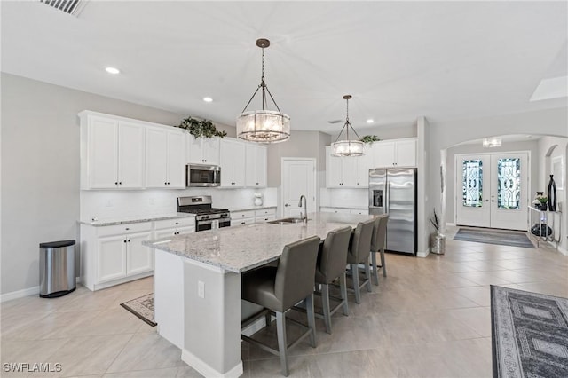 kitchen with arched walkways, appliances with stainless steel finishes, a sink, french doors, and backsplash