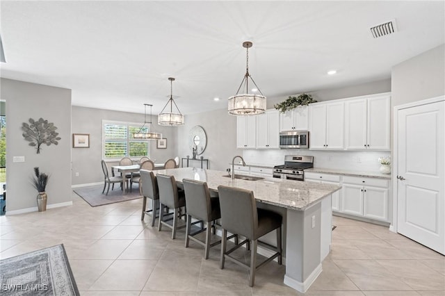 kitchen with light tile patterned floors, stainless steel appliances, a sink, visible vents, and a kitchen bar