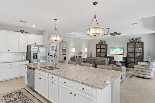 kitchen featuring arched walkways, a center island with sink, a raised ceiling, appliances with stainless steel finishes, and a sink