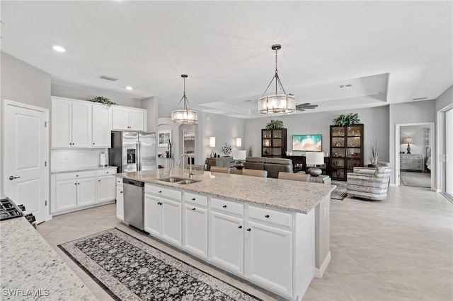 kitchen with stainless steel appliances, a tray ceiling, a sink, and a kitchen island with sink