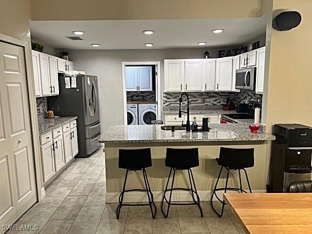 kitchen with stainless steel appliances, light stone countertops, independent washer and dryer, a peninsula, and a kitchen bar