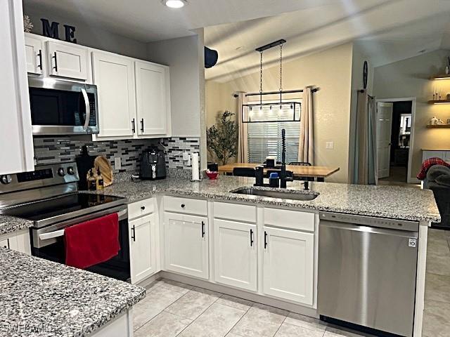 kitchen with light stone counters, stainless steel appliances, white cabinetry, a sink, and a peninsula