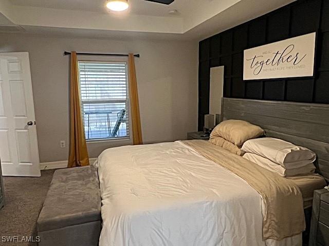 bedroom featuring a ceiling fan, a tray ceiling, carpet flooring, and baseboards