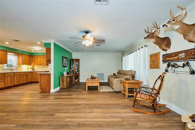 living area with light wood finished floors, baseboards, visible vents, and crown molding