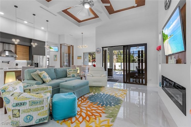 living room featuring ceiling fan with notable chandelier, a high ceiling, coffered ceiling, a fireplace, and beam ceiling