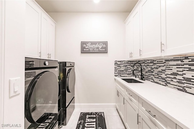 clothes washing area featuring light tile patterned floors, washing machine and dryer, a sink, baseboards, and cabinet space