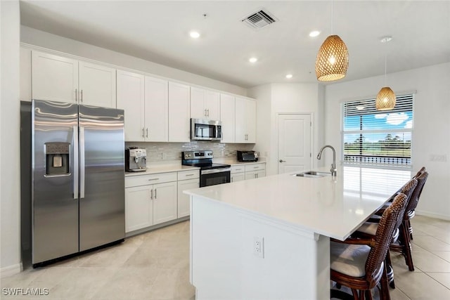 kitchen featuring stainless steel appliances, tasteful backsplash, visible vents, white cabinetry, and a sink