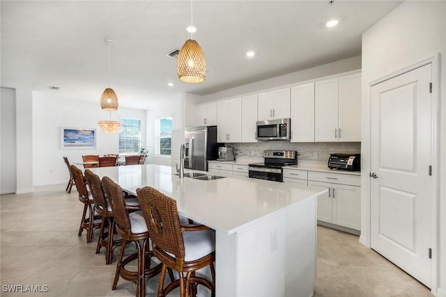 kitchen with a kitchen island with sink, stainless steel appliances, a sink, a kitchen breakfast bar, and tasteful backsplash