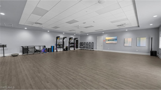 interior space with a tray ceiling, a paneled ceiling, visible vents, wood finished floors, and baseboards