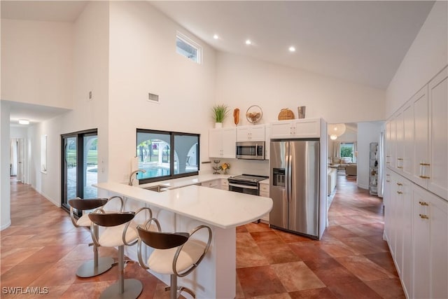 kitchen featuring a peninsula, a kitchen breakfast bar, white cabinets, stainless steel appliances, and a sink