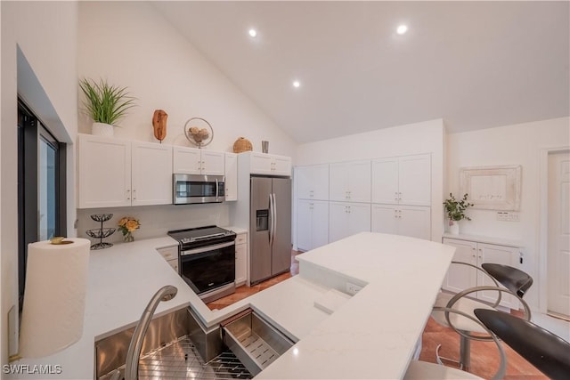 kitchen featuring white cabinetry, light countertops, appliances with stainless steel finishes, a kitchen breakfast bar, and high vaulted ceiling