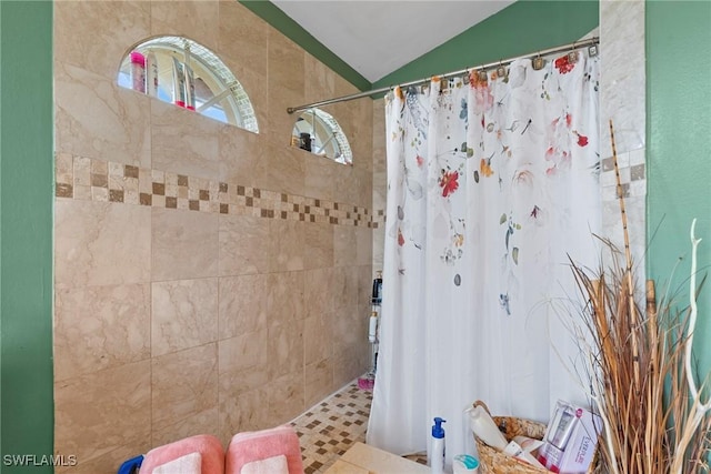 bathroom with a tile shower and lofted ceiling