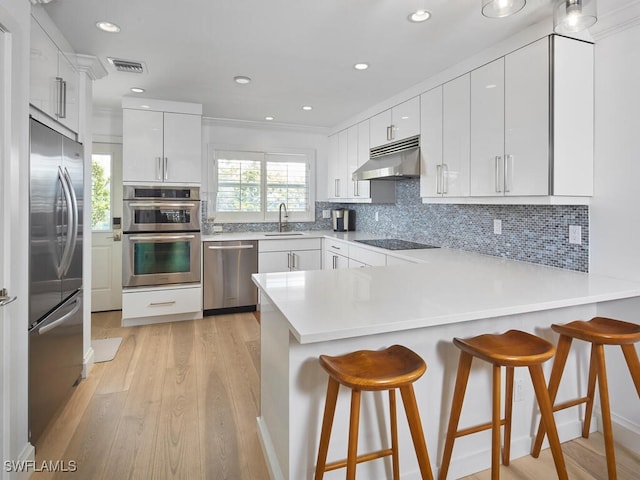 kitchen with visible vents, appliances with stainless steel finishes, a peninsula, under cabinet range hood, and a sink