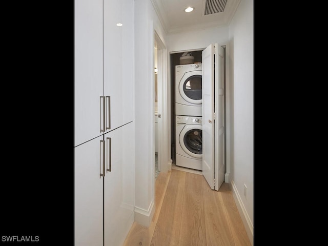 washroom with crown molding, visible vents, stacked washing maching and dryer, light wood-type flooring, and laundry area