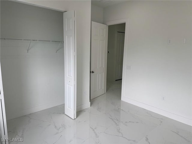 unfurnished bedroom with baseboards, marble finish floor, and a closet