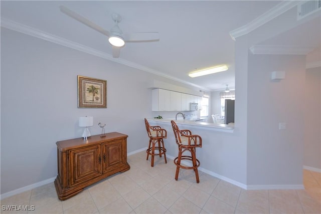 kitchen featuring visible vents, white microwave, ornamental molding, a kitchen bar, and light tile patterned flooring