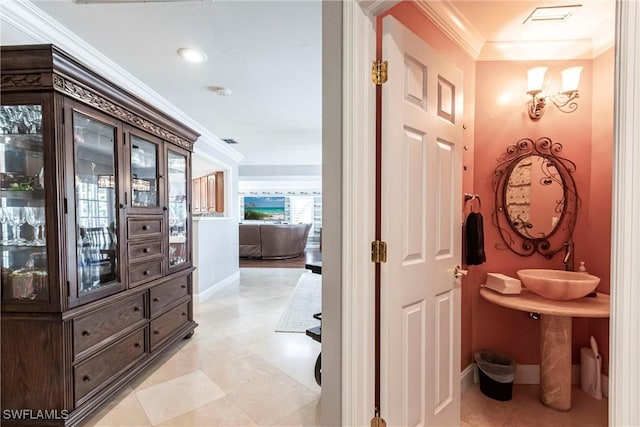 hall featuring baseboards, a sink, visible vents, and crown molding