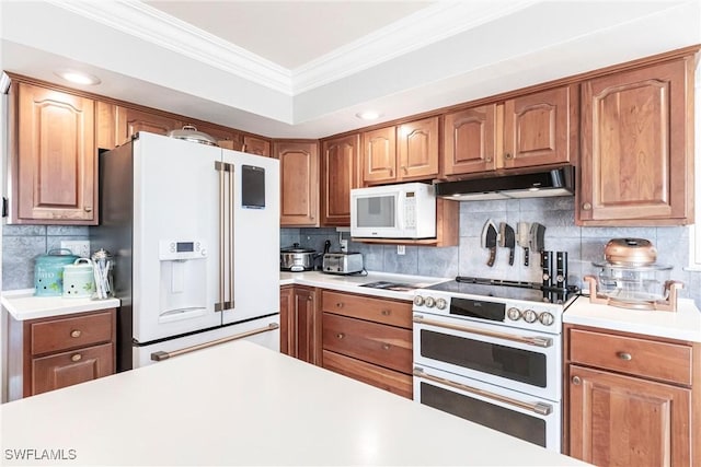 kitchen featuring under cabinet range hood, white appliances, light countertops, tasteful backsplash, and crown molding