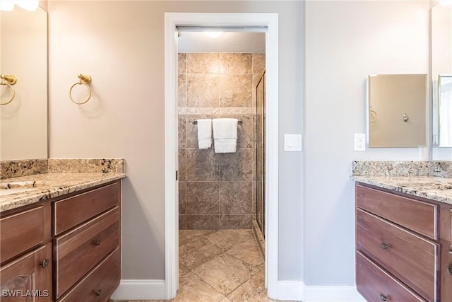 full bathroom featuring two vanities, a shower stall, and baseboards