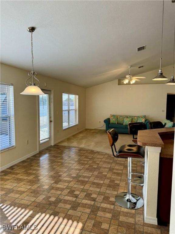 unfurnished living room with vaulted ceiling, a ceiling fan, visible vents, and baseboards