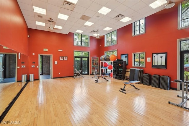 exercise room with a high ceiling, a paneled ceiling, wood-type flooring, and visible vents