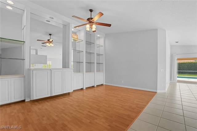 empty room with baseboards, light wood finished floors, a ceiling fan, and built in features