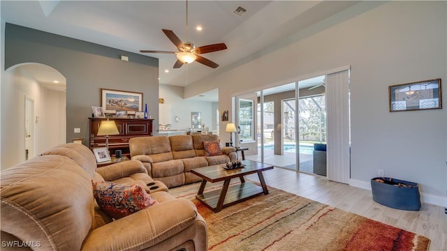 living room featuring arched walkways, visible vents, baseboards, a ceiling fan, and light wood finished floors