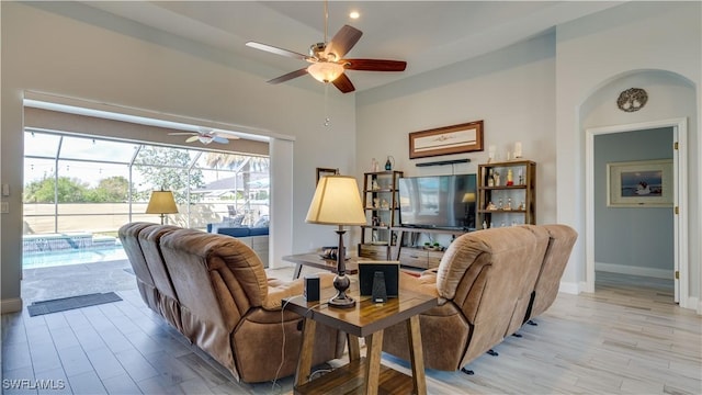 living room with light wood-type flooring, a ceiling fan, and baseboards