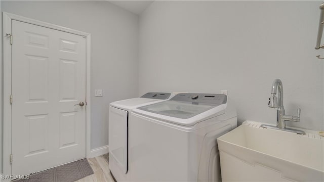 clothes washing area with washing machine and dryer, laundry area, a sink, and light wood-style flooring