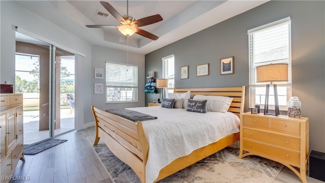 bedroom featuring visible vents, baseboards, light wood-style floors, access to outside, and a tray ceiling