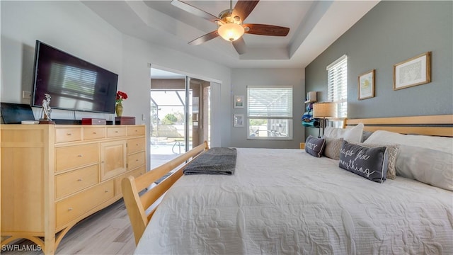 bedroom featuring access to exterior, light wood-style flooring, a raised ceiling, and ceiling fan