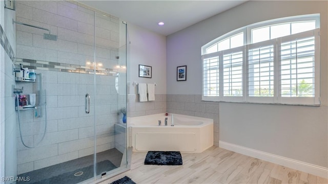 full bathroom featuring a healthy amount of sunlight, a garden tub, a shower stall, and baseboards