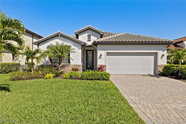 mediterranean / spanish-style home featuring an attached garage, stone siding, decorative driveway, stucco siding, and a front lawn