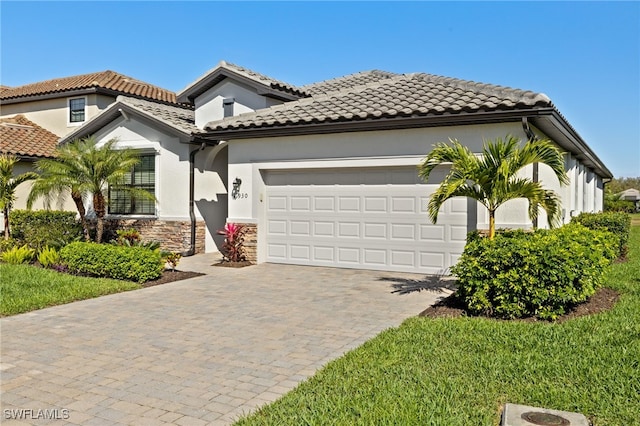 mediterranean / spanish home with stone siding, a tiled roof, an attached garage, decorative driveway, and stucco siding