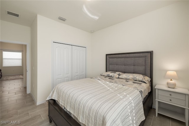 bedroom with wood finish floors, a closet, visible vents, and baseboards