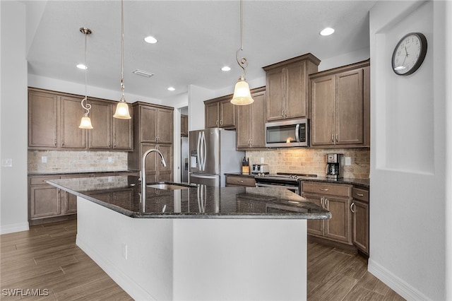 kitchen featuring dark wood-type flooring, a center island with sink, stainless steel appliances, and a sink