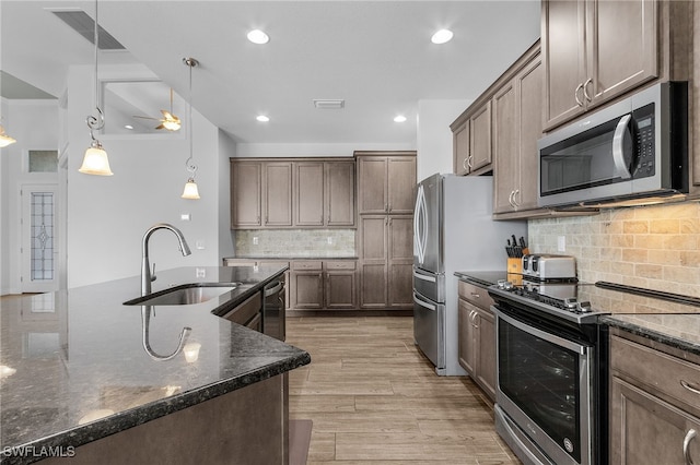 kitchen featuring stainless steel appliances, visible vents, a sink, dark stone countertops, and light wood-type flooring