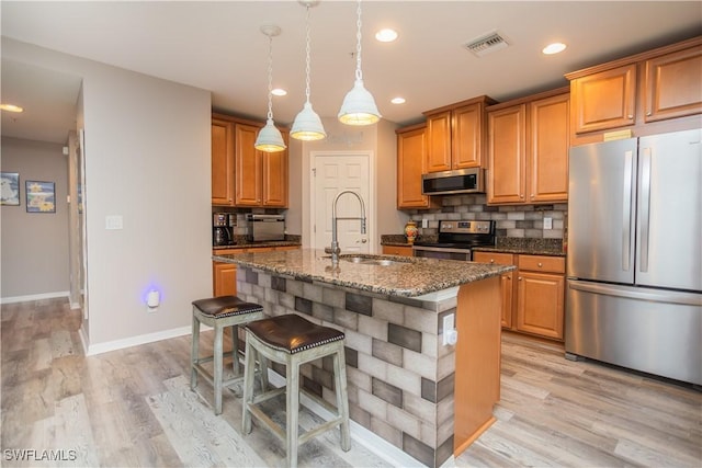 kitchen featuring a center island with sink, visible vents, dark stone counters, stainless steel appliances, and a sink