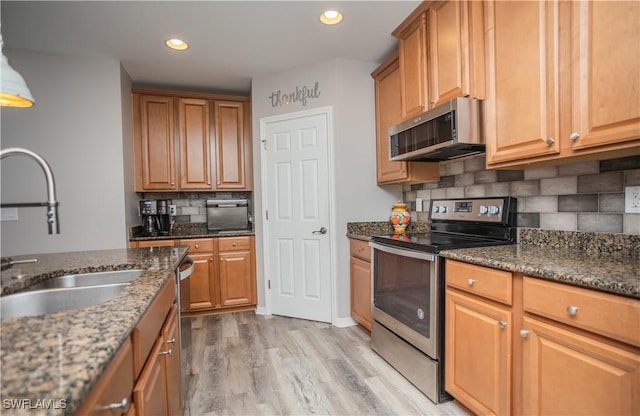 kitchen featuring light wood-style floors, appliances with stainless steel finishes, dark stone counters, and a sink